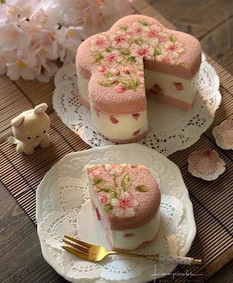 Heart-shaped pink floral cake with a slice on a white plate and a small bear figurine