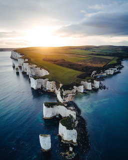 Aerial photograph of white chalk cliffs jutting into turquoise ocean at sunset with green farmland on top