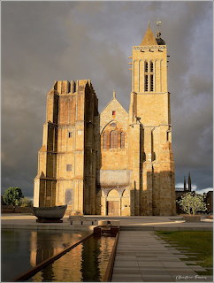 Gothic cathedral with tall tower lit by golden sunlight against dark storm clouds with water reflection