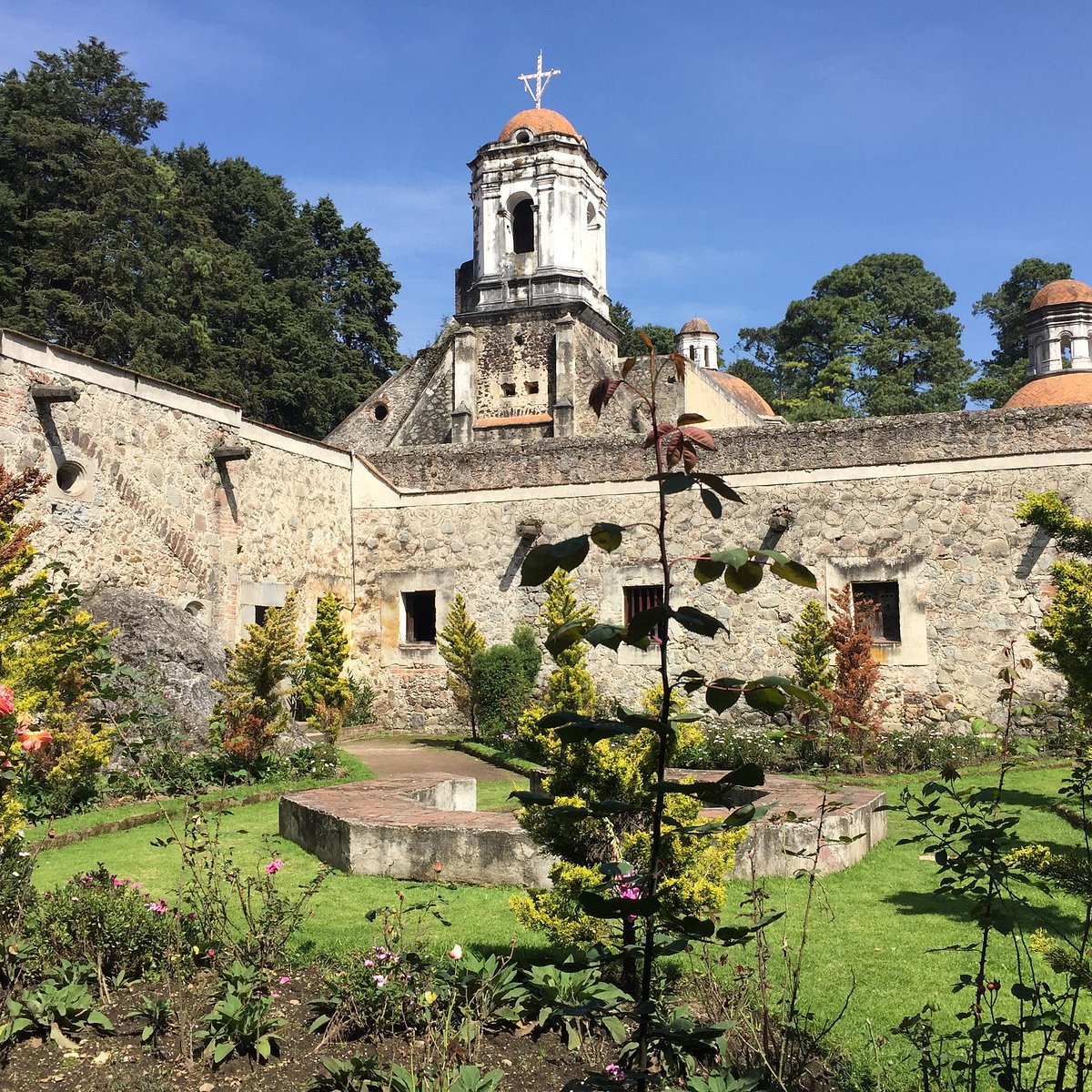 Historic stone convent with bell tower and cross above garden courtyard with sculpted trees