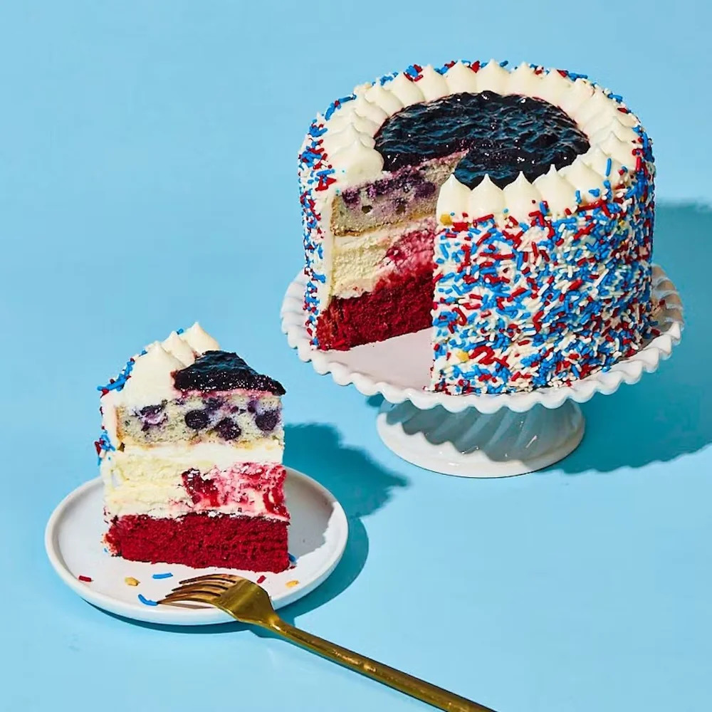 Slice of red, white and blue layered cake with sprinkles on turquoise background
