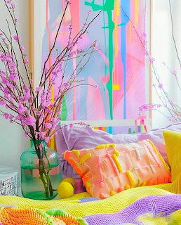 Colorful bedroom corner with rainbow wall art, bright cushions, neon yellow and pink bedding, and decorative pink branches