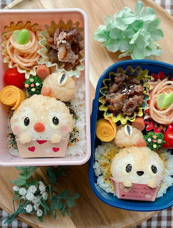 Two bento boxes with kawaii character food art, decorated rice shapes, pastries, and colorful fruit arrangements