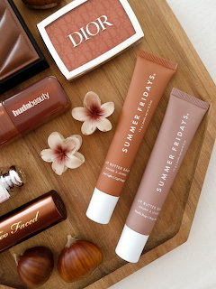 Brown makeup products and skincare arranged on wooden board with flowers and clips