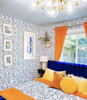 Colorful bedroom with blue patterned wallpaper, blue velvet bed, orange curtains and gold chandelier