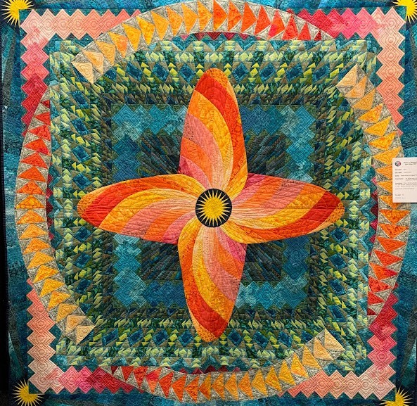 Handmade quilt with orange star mandala radiating outward, surrounded by teal feathers and rainbow scalloped borders