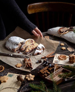 Christmas stollen bread with powdered sugar, cinnamon sticks, and holiday cookies on wooden table