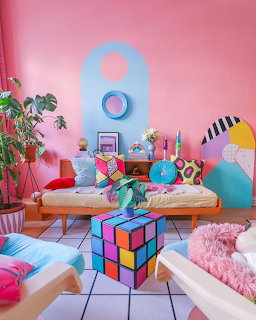 Bright pink living room with colorful cushions, Rubik's cube coffee table, and eclectic retro decor