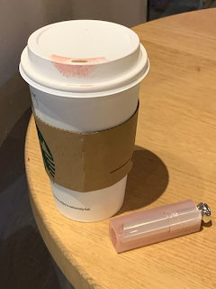 White takeaway coffee cup and pink lip gloss on a wooden table