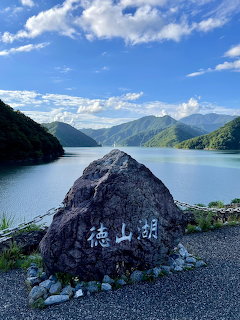 Stone monument with Japanese kanji in front of Tokuyama Lake surrounded by green mountains