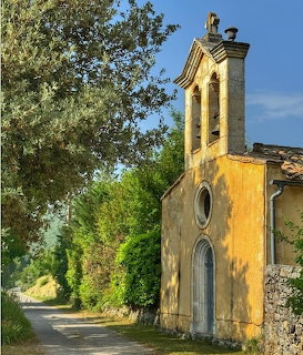 Small yellow chapel beside a narrow country road with trees and blue sky
