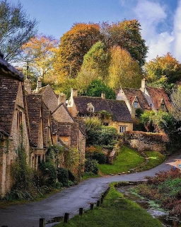 Stone cottages along a winding village road beneath tall autumn trees