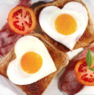 Two heart-shaped fried eggs on toast with bacon and tomato slices on white plate