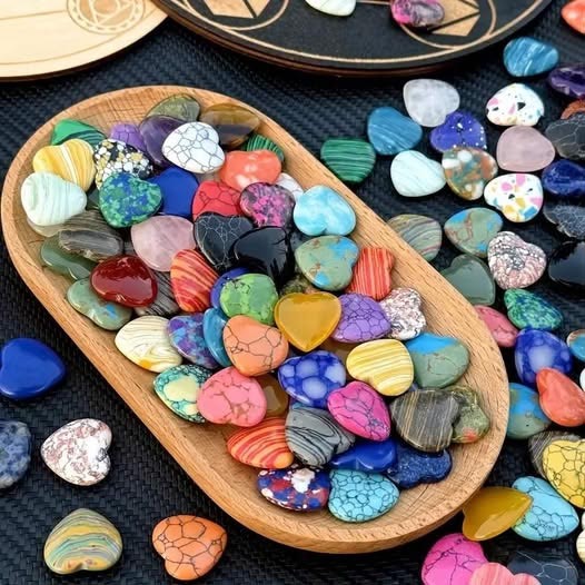Wooden tray filled with colorful heart-shaped stones on a dark surface