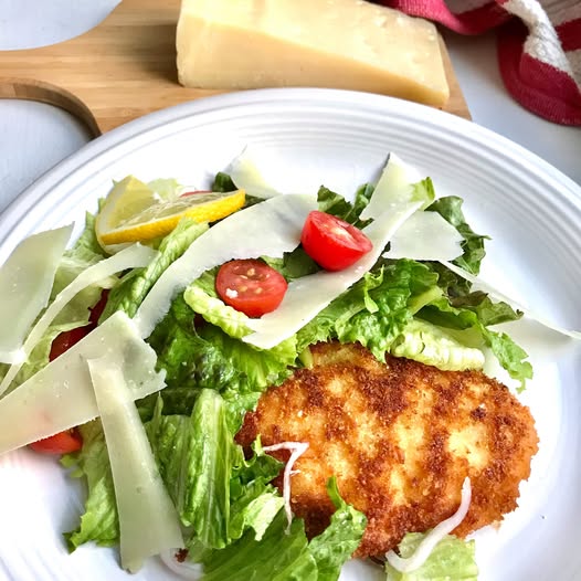 Fresh salad with shaved cheese, cherry tomatoes, and a breaded cutlet on a white plate