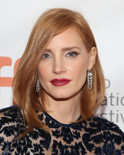 Portrait of a red-haired woman with red lipstick and crystal earings in a dark embroidered dress