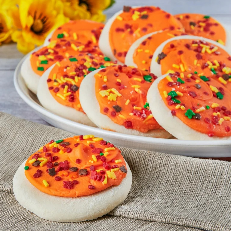 Round sugar cookies with orange frosting and red, yellow, green sprinkles on white plates