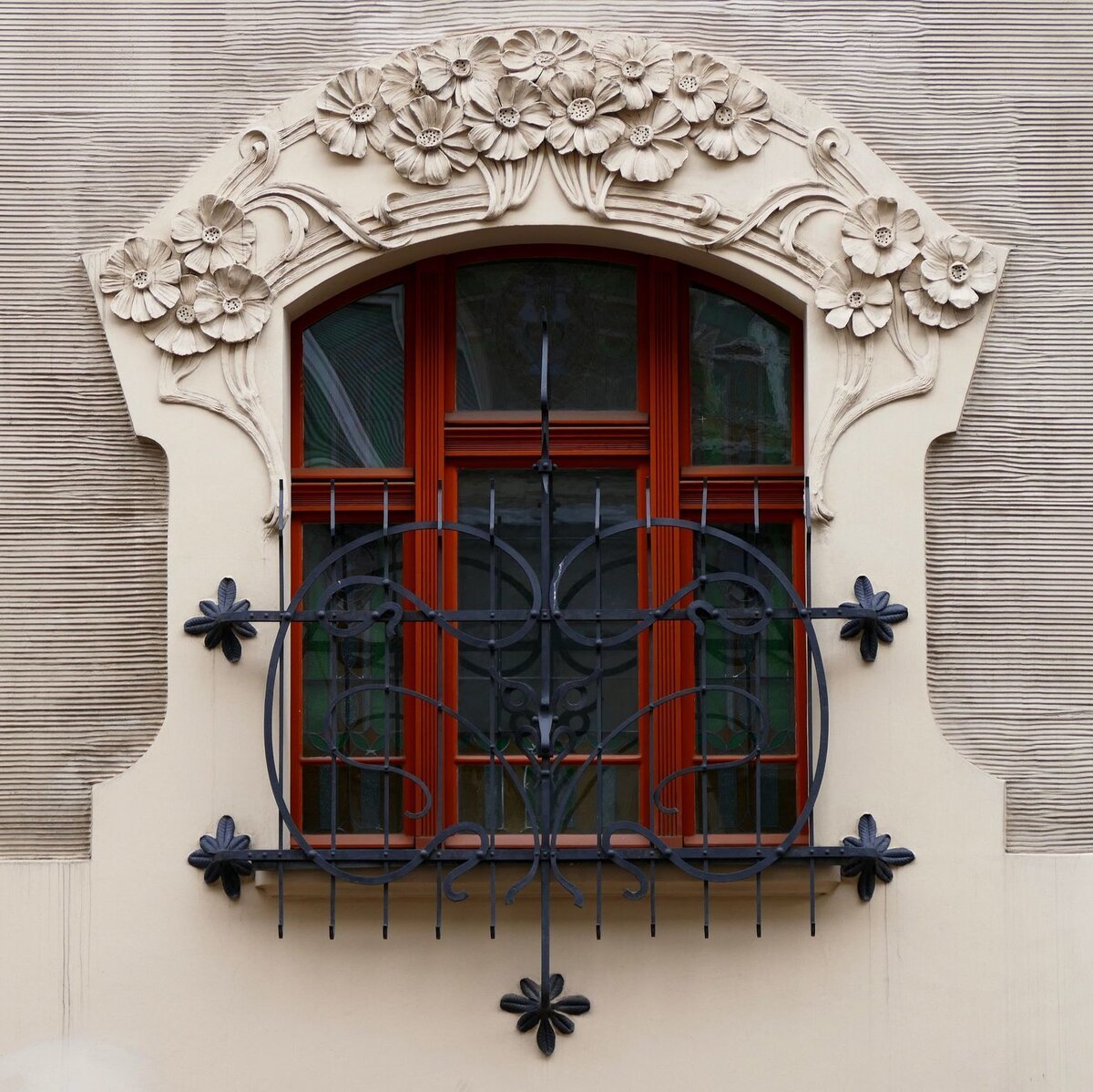 Ornate arched window with floral stone carvings, iron bars, and a small balcony