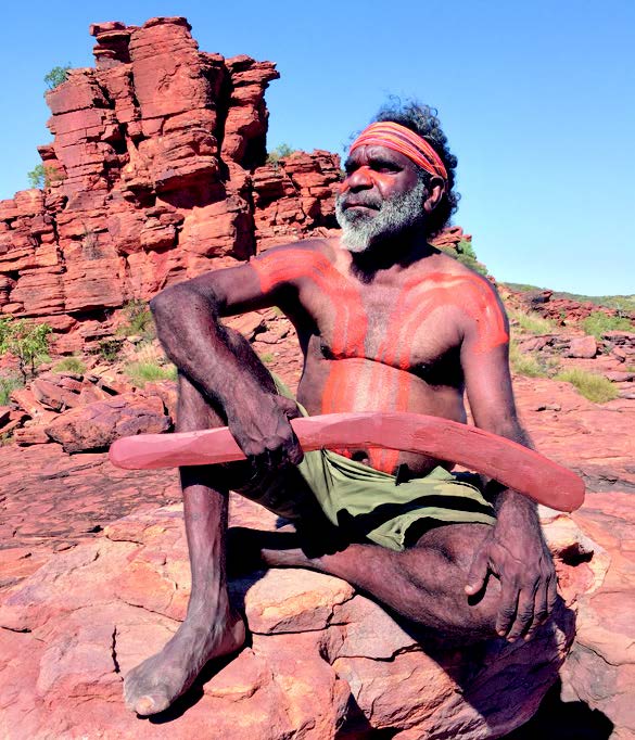 Aboriginal man with body paint holding boomerang in Australian outback