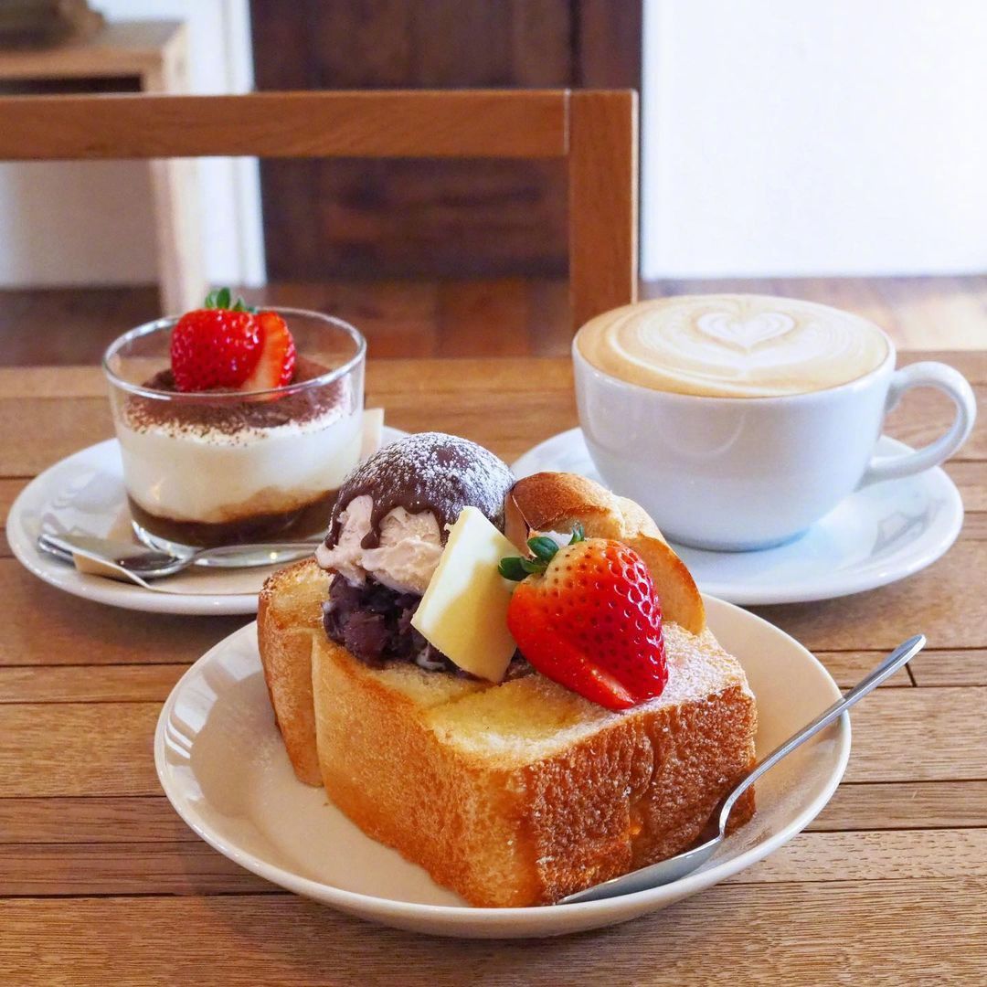 Honey toast with fruit and ice cream, a latte, and a small dessert on a wooden table