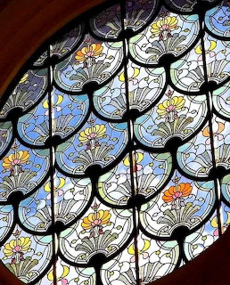 Art Nouveau stained glass window with repeating floral fan-shaped patterns in blue, green, and orange