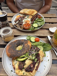 Breakfast sandwich with avocado, egg, and grilled meat on a plate at an outdoor table
