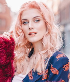 Woman with long pink wavy hair and blue eyes wearing floral top, soft outdoor portrait