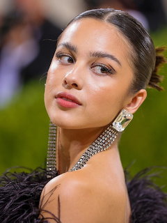 Young woman with slicked-back hair wearing crystal choker necklace and diamond earings in black feathered dress