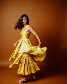 Woman in bright yellow dress twirling gracefully against orange studio background