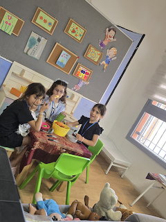 Children and teacher at a green table in a colorful classroom with framed artwork on walls