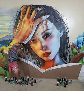 Large graffiti mural showing a woman's face with her hand on her forehead, spray paint cans at the base