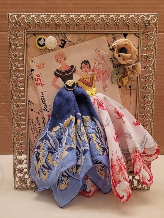 Two handmade fabric dolls in blue and pink dresses leaning against a decorative gold picture frame