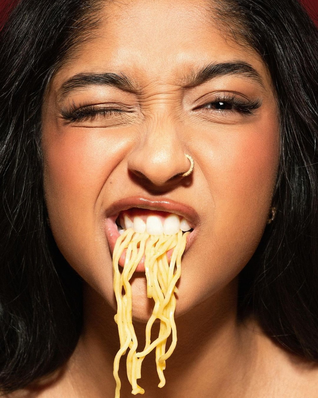 Close-up of a woman winking with noodles hanging from her mouth