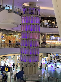 Purple illuminated Leaning Tower of Pisa replica inside a multi-story shopping mall