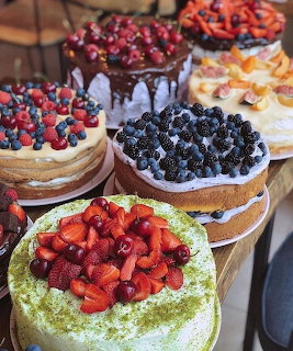 Assorted cakes topped with fresh fruits including strawberries, blueberries, raspberries, and figs