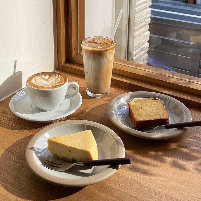 Cafe table by a window with coffee, cake, and toasted bread on white plates