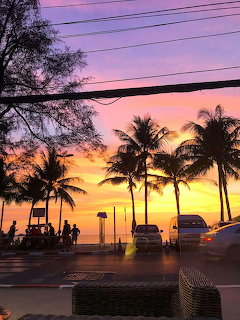 Palm trees silhouetted against colorful sunset sky on coastal road with cars and people