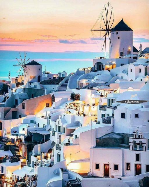 White windmills and buildings of Santorini village at sunset with pink and blue sky over the sea