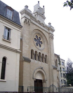 Stone facade of Versailles Synagogue with rose window, arched doorway, and square tower