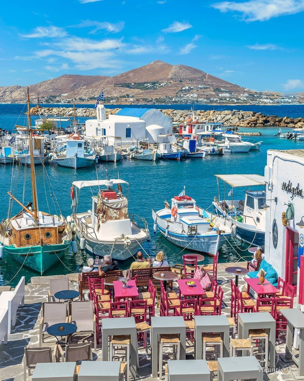 Colorful fishing boats in a Greek island harbor with white buildings and a hillside in the background