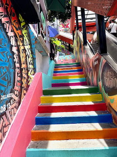 Colorful outdoor stairway with rainbow-painted steps and vibrant street art murals on surrounding walls