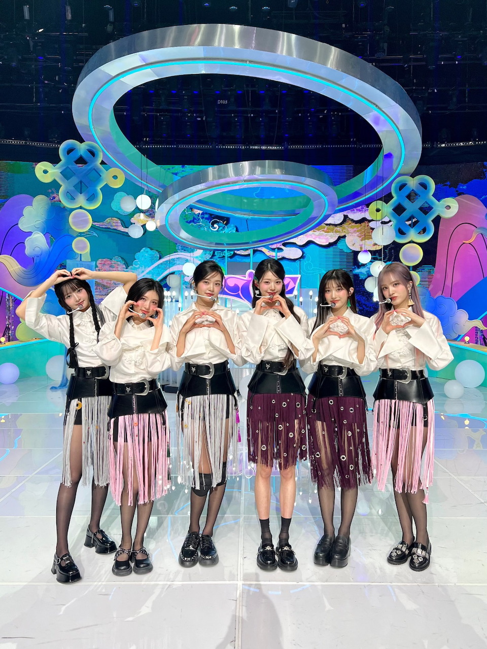 Six female K-pop idols from IVE posing together on a vibrant colorful stage set