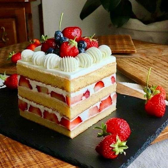 Layered cream cake with strawberries, blueberries, and raspberries on a black serving board