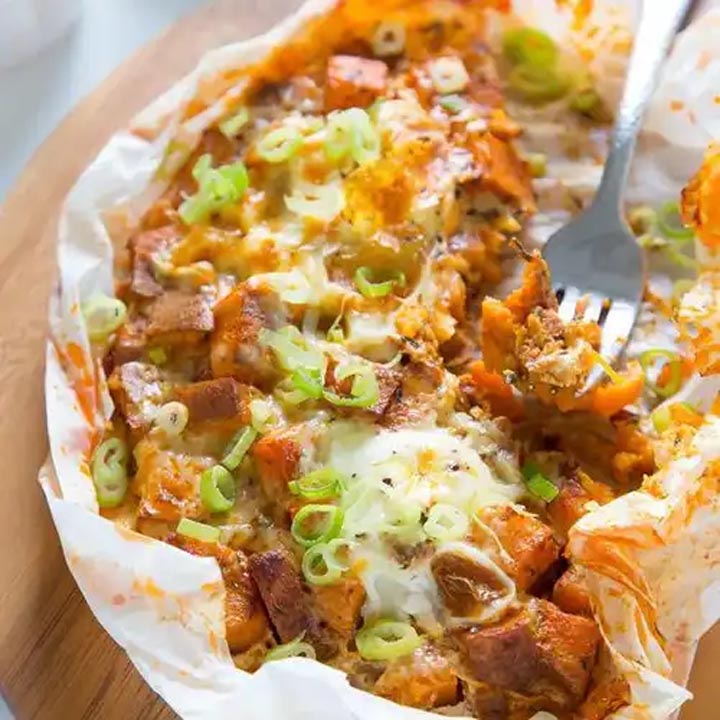 Baked sweet potato topped with melted cheese, bacon, and green onions on parchment paper
