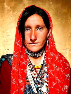 Woman in red headscarf with layered silver necklaces and traditional jewelry against textured gold background