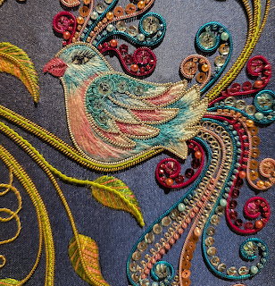 Detailed embroidered bird with turquoise and coral colors, decorative swirls, beads and golden threads on navy fabric