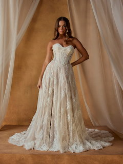 Woman in strapless lace wedding dress with long train posing against draped curtain backdrop