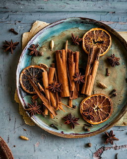 Cinnamon sticks, dried orange slices, and star anise on a turquoise plate on rustic blue wood background