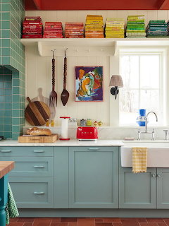 Teal kitchen cabinets with white counters, green subway tile, and rainbow-arranged books on shelf above