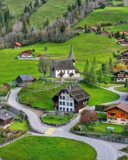 Aerial view of Swiss alpine village with white church surrounded by green meadows and traditional chalets
